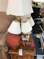Five assorted lamps displayed including a brass lamp, two lamps with pleated white shades, and a red lantern style lamp with red shade.