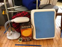 Photo showing the white sunlamp with flexible hose, blue gel pad, original Sunlamp Kit box, small metal tin with green label, and a metal walking aid.