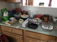 Full view of plastic kitchenware collection including containers, plates, platters, butter tray, and kitchen accessories on countertop near cabinets.