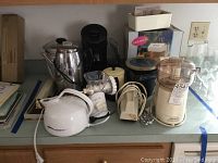 Overall view of the kitchen counter showing all kitchen items including juice extractor, Fry Baby deep fryer, teapots, rice cooker and more