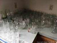 Variety of clear glassware items arranged on a counter including tumblers, small glass bowls, shot glasses, and wine glasses.