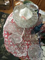 Photo showing large cut glass punch bowl with ladle, surrounded by smaller cups and assorted glass serving dishes on a red patterned tablecloth.