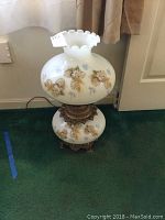 Full view of the white milk glass lamp with floral designs on top shade and base, and visible electric cord.