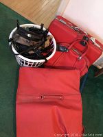 Large red suitcase, carry-on bag, suit bag, and white laundry basket with multiple purses arranged on floor