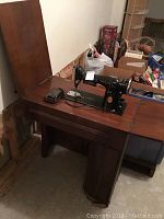 Vintage black Singer sewing machine with gold accents placed on a wooden table showing the sewing machine and table top.