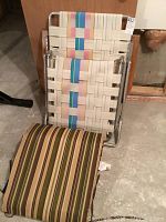 Adjustable lawn chair with woven strap seating and separate brown striped cushion on concrete floor.