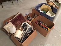 Full view of the lot showing boxes and bins filled with various household items including rugs, Mr. Coffee machine, office supplies, and kitchenware.