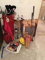 Wide view showing red fabric golf bag with clubs inside, umbrella in side pocket, metal pull cart with wheels and handle, and a white basket containing golf accessories and other items.