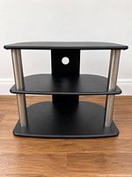 Front view of black three-tier TV stand with metal supports and cable cutout