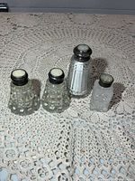 Group of four glass shakers standing on lace surface