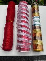 Front view of three deco mesh rolls: solid red, red/white stripe, sealed gold/copper checker