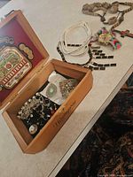 Overview of cigar box with jewelry, rosary, headbands, watch, necklace visible