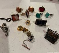 Group view of cufflinks, tie clip, tie tack, pins and tool on tabletop