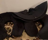 Two black U-shaped travel pillows and black boonie hat on floor