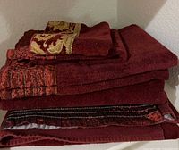 Stack of burgundy towels showing variety of sizes and embroidered trims