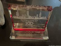 Front view of clear glass/acrylic plaque with red accents showing etched skyline and centennial inscription