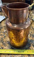 Full view of copper pitcher showing hammered texture, brass handle partially visible, tape for scale