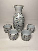 Front view of porcelain tokkuri carafe with four matching cups displaying blue floral vine pattern