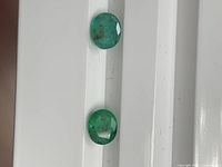 Pair of oval emeralds on white surface showing color and inclusions