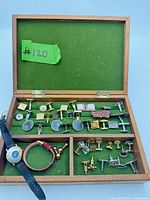 Open wooden box showing cufflink rows, wristwatch, bracelet and loose accessories