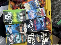 Overview of seven Clive Cussler paperbacks in yellow bin