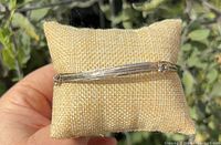 Front view of the multi-strand silver-tone bangle resting on a display pillow