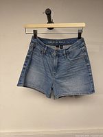 Front view of denim shorts hanging on hanger