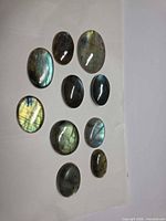 Ten oval labradorite cabochons arranged on white background showing various flashes