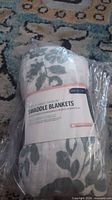 Packaged muslin swaddle blanket showing floral pattern and label
