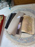 Stacked items on round floral rug including rolled tan runner, brown easyLiner shelf liner, small pastel rug and dark mat