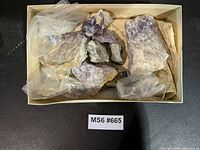 Top view of cardboard tray containing multiple rough amethyst pieces with packaging material