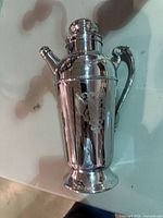 Full view of shaker front showing handle, spout and engraved motif