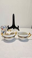 Covered sugar bowl with lid and creamer beside a beverage can for scale, display stand in background