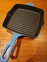 Angled view of blue-handled square grill pan showing ridged black interior