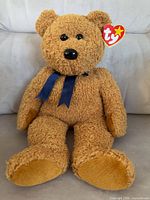 Front view of light brown Ty Beanie Buddy Fuzz bear with Ty tag and blue ribbon