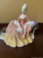 Front view of bone china figurine seated on chaise holding book