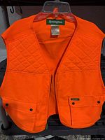 Front view of blaze orange Remington hunting vest showing quilted shoulders, pockets, and size tag