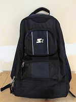 Front view of black Starter backpack showing logo pocket, lower compartment, zippers and overall wear