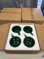 Open shipping box showing four green mugs seated in foam insert