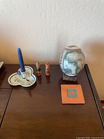 Lot overview showing globe egg, candle holder with candle, two figurines, fish tile on table