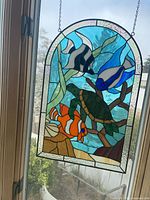 Full view of stained glass panel hanging in window showing overall design and attached chain