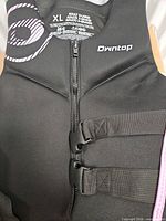 Front of black Owntop life jacket showing zipper, twin buckles, size label