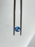 Round blue sapphire shown in tweezers against neutral background