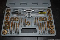 Open gray plastic case showing full tap and die set with taps, dies, wrench, die stock, and screwdriver