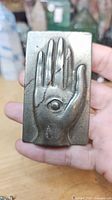 Front view showing raised hand and eye design on rectangular plaque