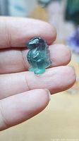 Front view of tiny green-purple fluorite animal figurine on fingertip