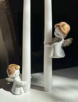 Two porcelain angel candle huggers attached to white taper candles