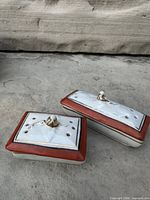 Pair of lidded porcelain boxes closed, showing perforated lids, rust borders and finials