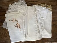 Stack of five folded white/ivory handkerchiefs showing varied trims and embroidery