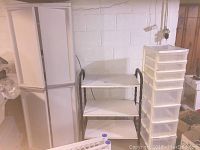 White plastic storage cabinet, formica table with metal frame, and plastic rolling cart with drawers shown together in basement setting.
